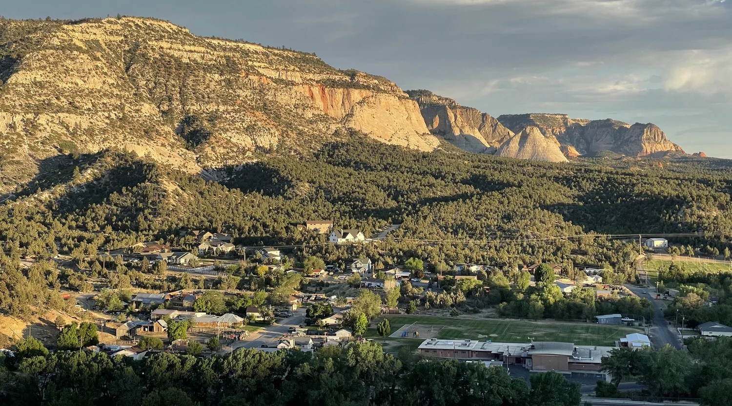 Golden-hour view of a small Southern Utah town beneath red sandstone cliffs along Highway 89