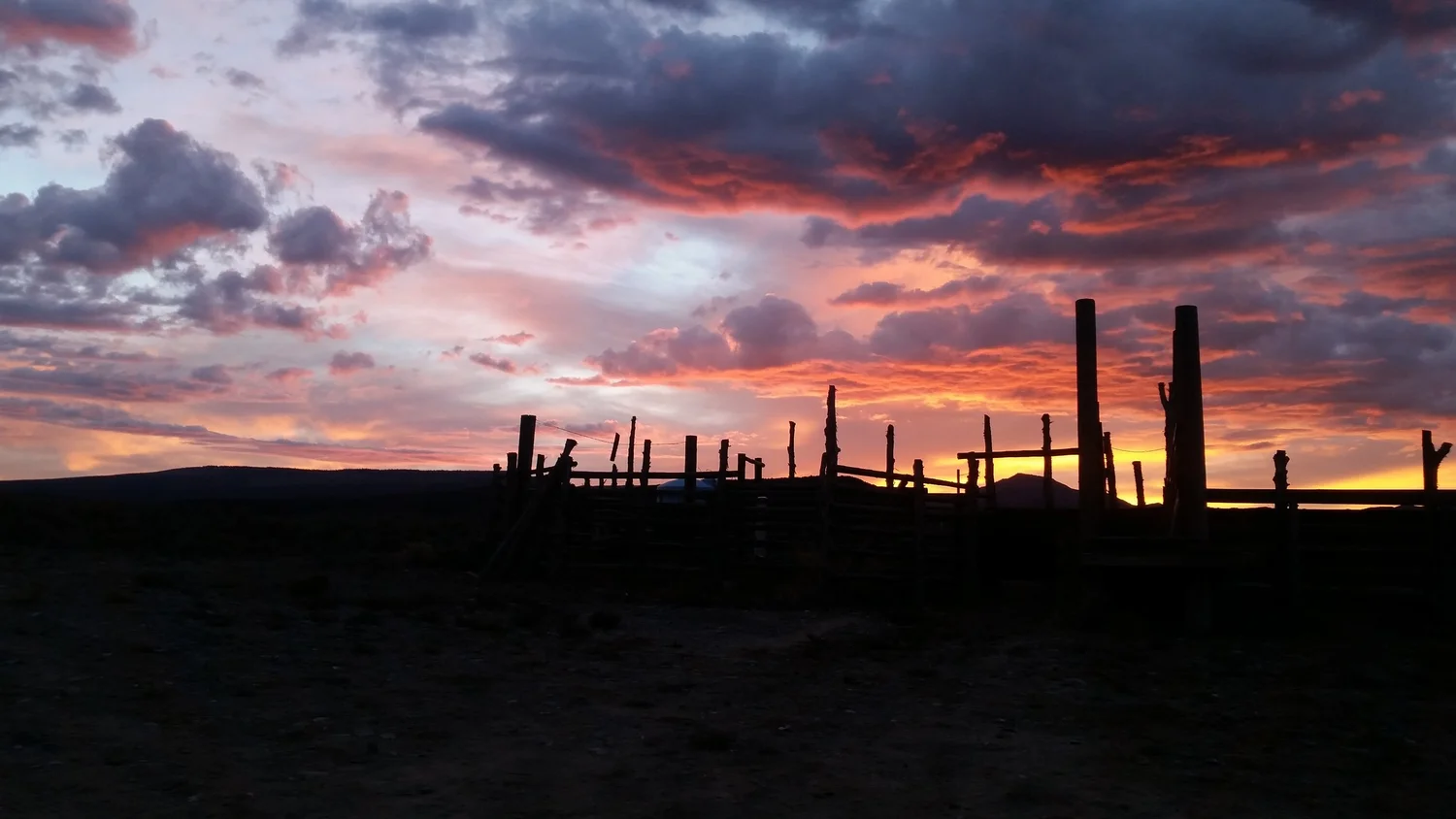 Sundown at the wooden corral along Highway 89, fence rails against an orange sky